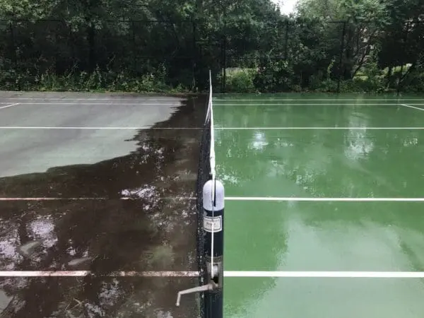 Tennis court showing dramatic contrast between dirty and cleaned surfaces during Aqua-Nomics professional pressure washing service