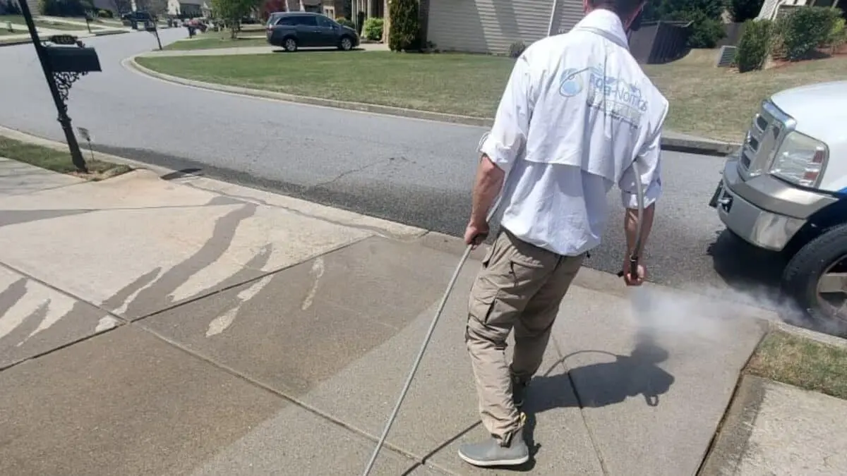 Technician pressure washing a dirty HOA sidewalk to reveal clean concrete, demonstrating difference between pressure and soft washing methods