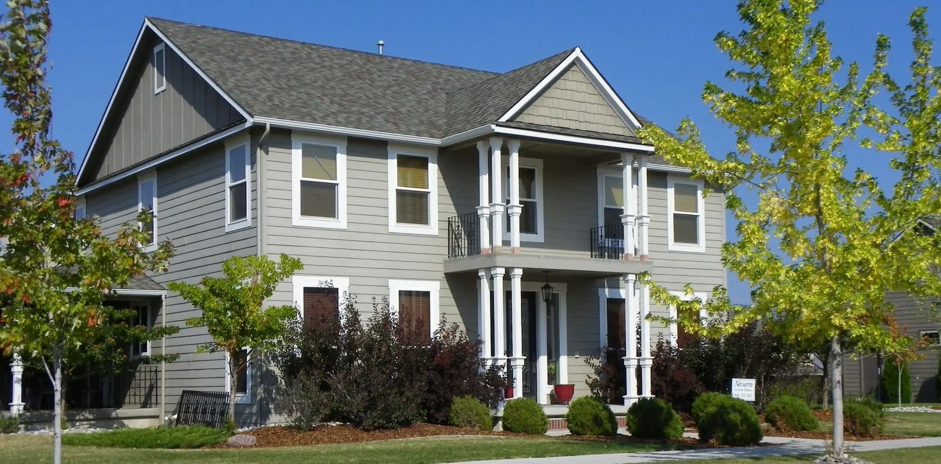 Stylish two-story home with freshly cleaned roof, crisp gray siding, white trim, and a tidy landscaped yard with trees and shrubs in early autumn colors