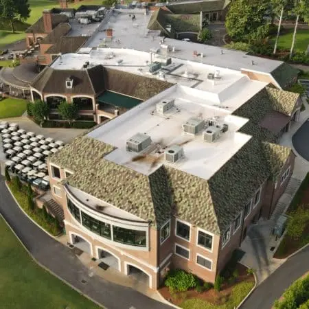 Overhead view of golf clubhouse with flat white roof in cleaning process, visible roof stains and equipment highlighting commercial pressure washing work