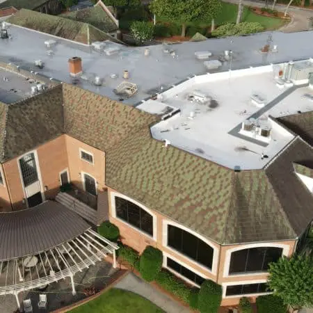Close aerial view of building with flat membrane and pitched shingle roof areas showing cleaning progress, rooftop HVAC units, and curved covered patio zone