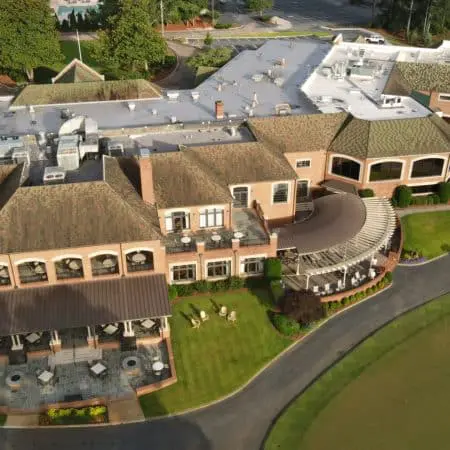 High-angle view of golf club facility with flat and pitched roofs, showing cleaned surfaces, outdoor patios, and organized cart storage in landscaped setting
