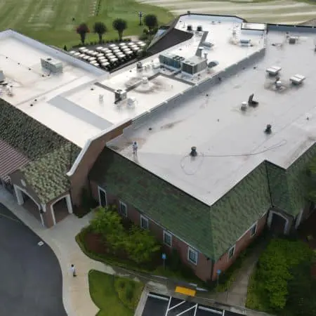 Aerial view of flat white membrane roof being pressure cleaned, with visible equipment and technicians removing dirt from a large commercial facility