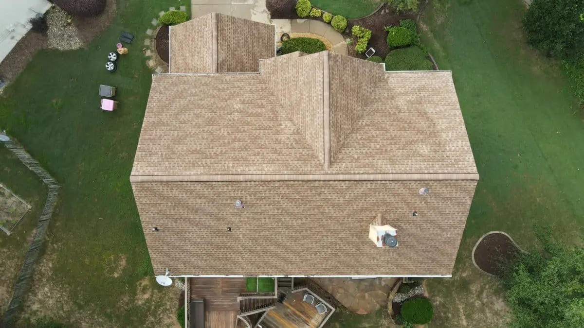 Top-down view of tan asphalt shingle roof in pristine condition after cleaning or installation, surrounded by lawn, landscaping, and wooden backyard deck