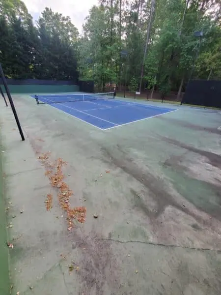 Dirty HOA Tennis Court Before Cleaning Heavily soiled HOA tennis court showing grime, stains, and leaf buildup before professional pressure washing to restore cleanliness and visual appeal