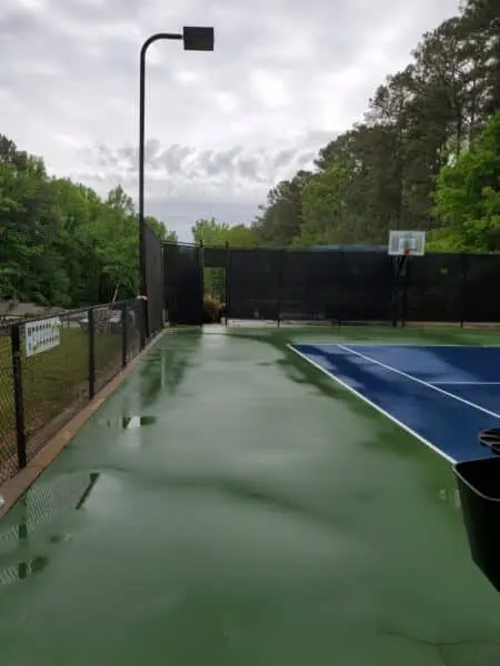 Clean Tennis Court Sidewalk View Freshly cleaned tennis court sidewalk with bright green surface and clear path after Aqua-Nomics pressure washing service