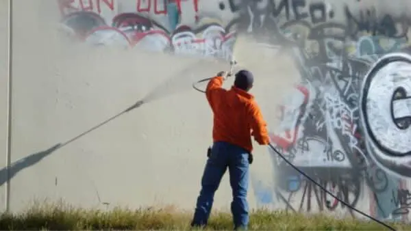 A technician power washes graffiti off a wall using high-pressure equipment. Learn expert tips on safe and effective graffiti removal with pressure washing