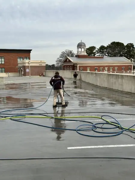 Team of pros pressure washing a rooftop parking deck to remove grime and buildup while improving surface safety and visual appeal for commercial property