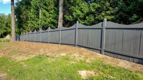 A sleek gray wooden fence with a scalloped top design, freshly painted and maintained, enhances the outdoor space with a clean, modern finish