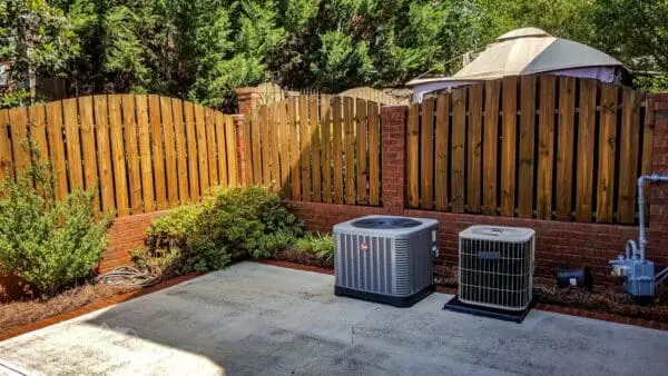 A restored wooden privacy fence with HVAC units shows the impact of expert cleaning, highlighting fresh wood tones and a spotless surrounding area